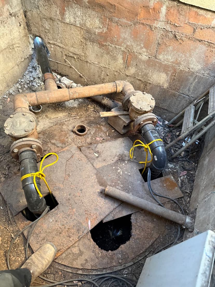 Industrial sump pump system with pipes and metal access cover in a construction site.